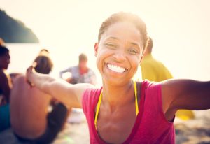 black woman on the beach with friends smiling and spreading her arms with joy while smiling at the camera